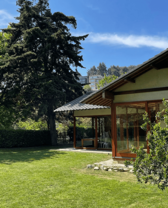 Büyük bir çam ağacının yanında duran geleneksel Japon tarzı ahşap ve cam pavyon.