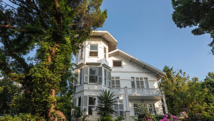 Açık mavi gökyüzü altında, doğayla iç içe geçmiş zarif tasarımlı beyaz ahşap köşk mimarisi.