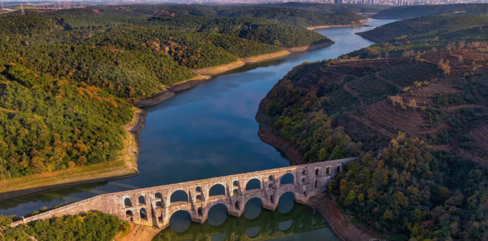 Ormanlık tepeler arasında kıvrılarak akan nehrin üzerindeki görkemli tarihi taş su kemeri ve durgun suya yansıması.
