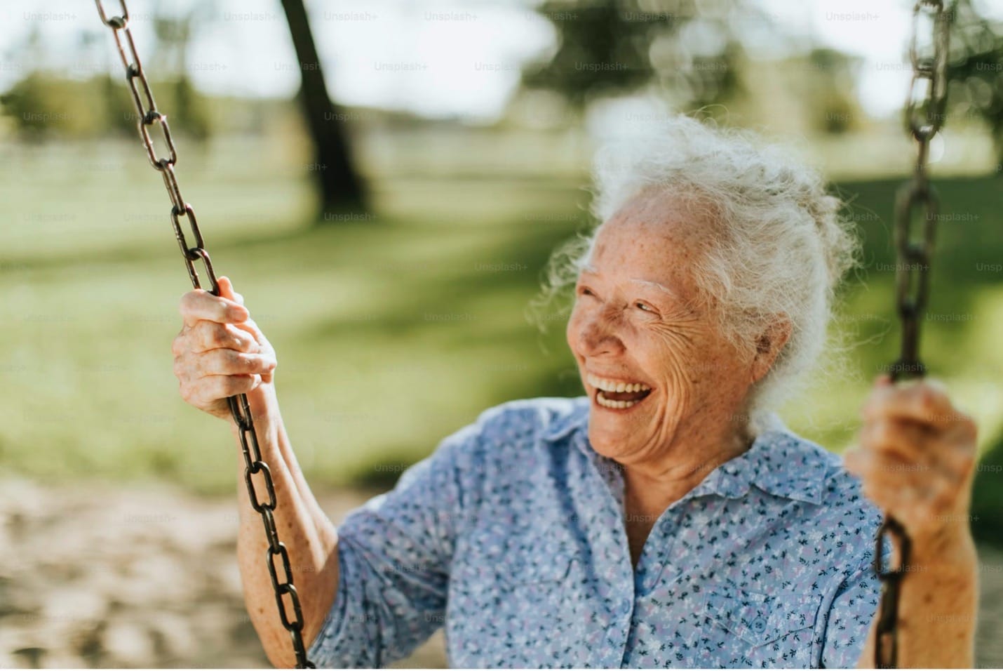 Cheerful senior woman with white hair laughing while enjoying a swing at a sunny park