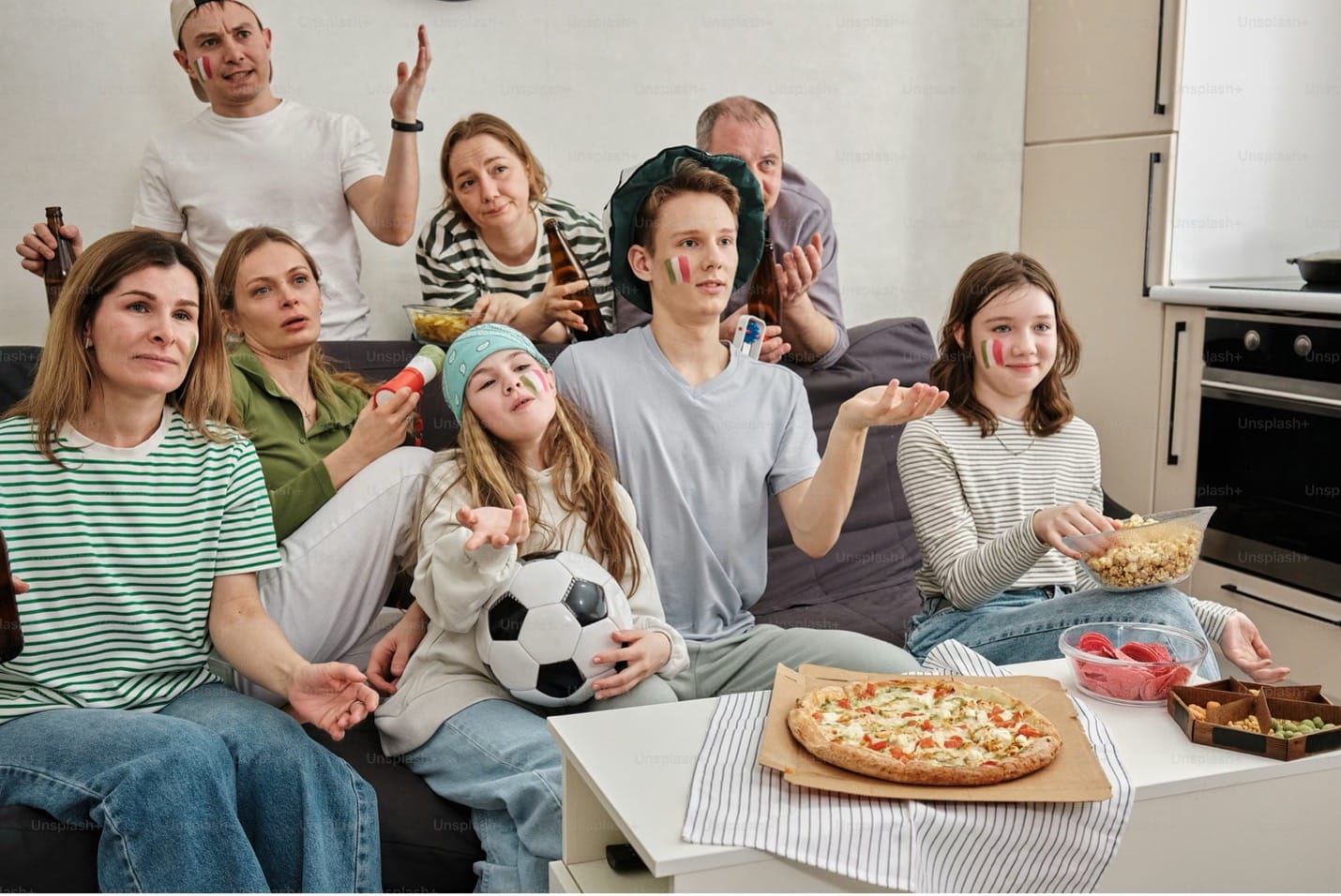 Group of sports fans in a living room with pizza, snacks, and Italian face paint watching a game.